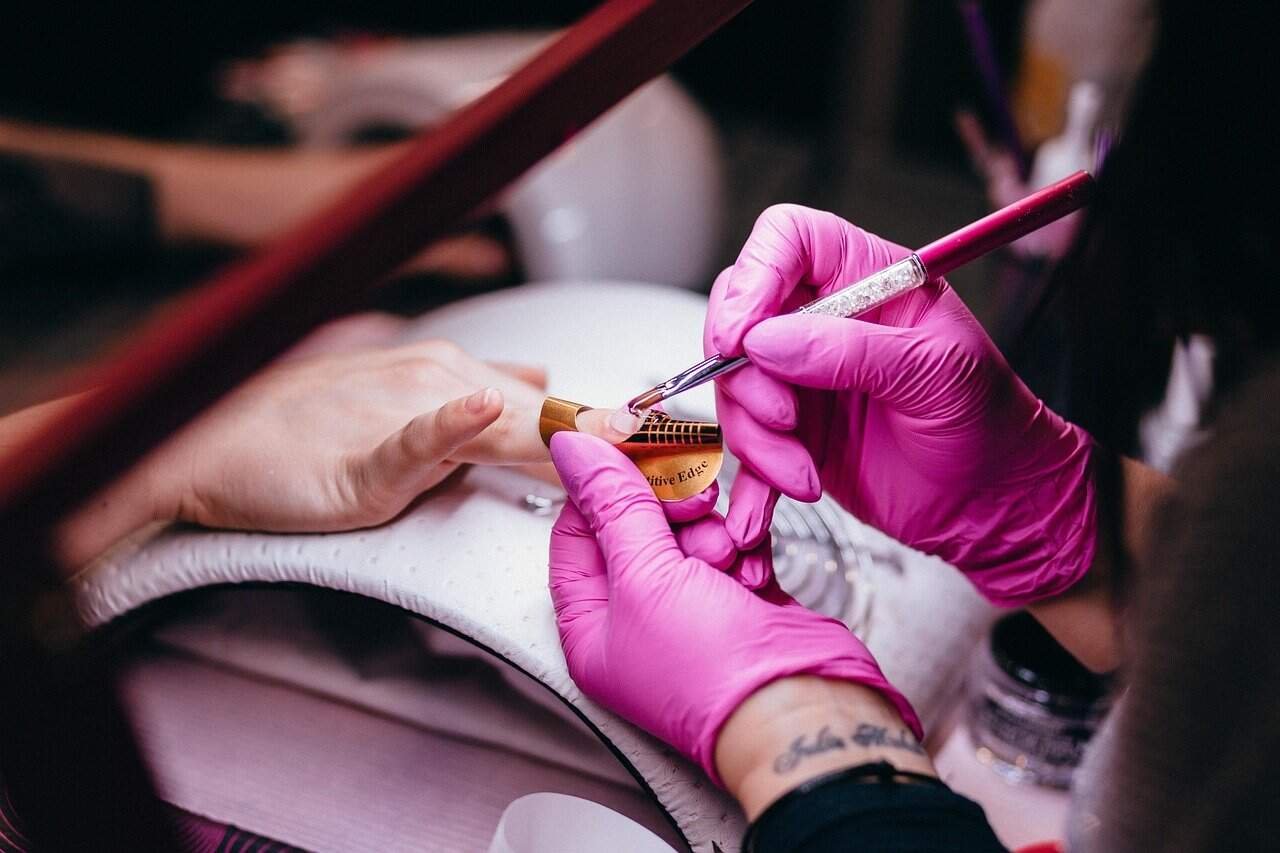 Utilizar guantes- Mujer joven usando guantes protectores mientras pinta las uñas
