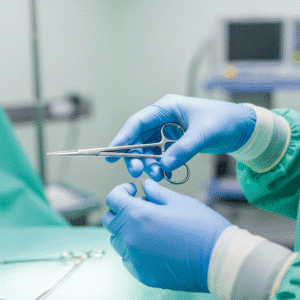 Manos de un médico con guantes quirúrgicos esterilizados, sosteniendo unas tijeras de cirugía para ilustrar el uso y la función de los guantes - Para qué sirven los guantes quirúrgicos